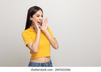 Excited Asian Woman Shout Out Loud Wow With Hands On Isolated Background. Happy Shocked Face Female Wow Promotion Advertising Concept. Joyful Teenage Girl In Yellow Shirt Standing In White Room.