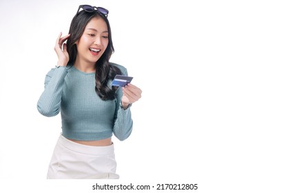 Excited Asian Woman With Sunglasses Looking Credit Card In Hand Standing On White Background. Cheerful Surprised Young Girl Holding Blank Card For Payment Online Over Isolated. Finance Shopping Online