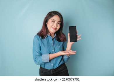 Excited Asian woman wearing blue shirt pointing at the copy space on her smartphone, isolated by blue background - Powered by Shutterstock