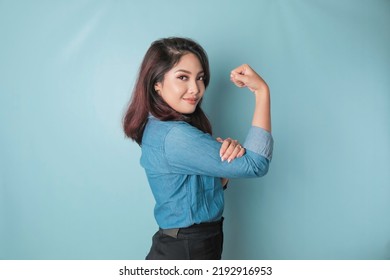 Excited Asian woman wearing a blue shirt showing strong gesture by lifting her arms and muscles smiling proudly - Shutterstock ID 2192916953