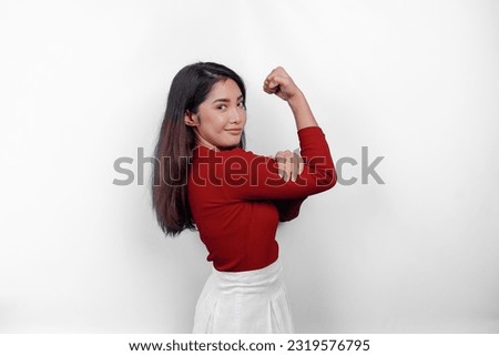 Excited Asian woman wearing a red top showing strong gesture by lifting her arms and muscles smiling proudly