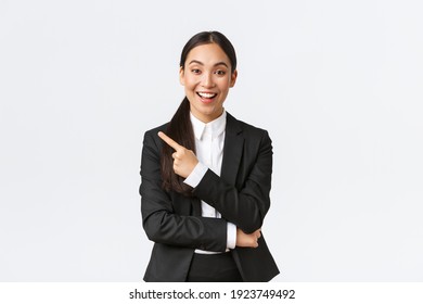 Excited attractive asian female saleswoman, real estate agent in suit suggesting perfect house, standing in suit and pointing finger left. Businesswoman making announcement, show banner