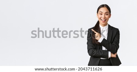 Excited attractive asian female saleswoman, real estate agent in suit suggesting perfect house, standing in suit and pointing finger left. Businesswoman making announcement, show banner