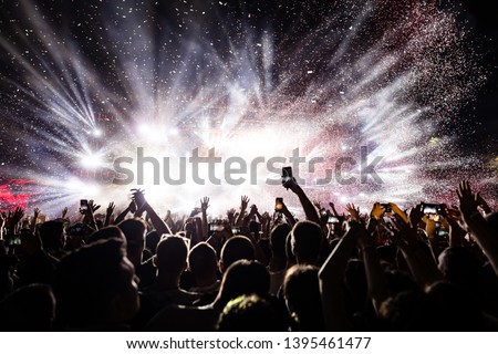 Excited audience watching confetti fireworks and having fun on music festival at night. Copy space. 