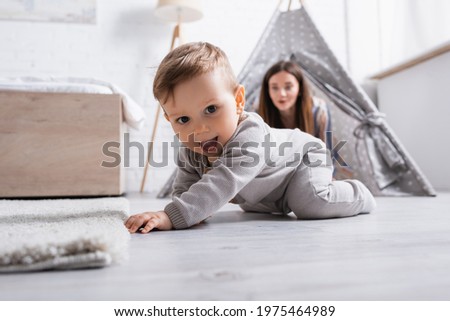 excited baby boy crawling on floor near mother on blurred background