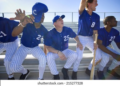 Excited Baseball Team Jumping Up From Bench In Stand During Competitive Baseball Game, Cheering, Front View (backlit)