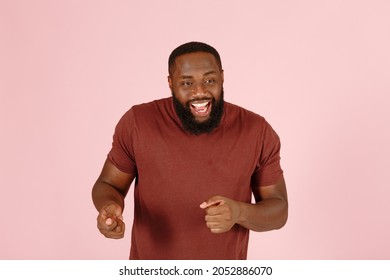 Excited bearded African-American guy actor in brown t-shirt dances standing on light pink background in studio close view - Shutterstock ID 2052886070