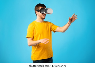 Excited bearded guy using VR headset and experiencing virtual reality, isolated on blue studio wall