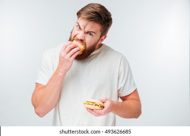 Excited bearded man greedily eating hamburgers isolated on white background