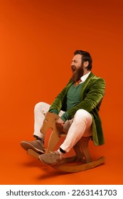 Excited bearded man in jacket sitting on rocking horse on red background