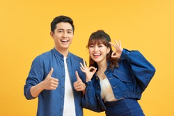 Excited Beautiful Asian Couple Shows Thumb Up Gesture Agree To Do Something And Collaborate Against Orange Wall, Did Great Job, Show Approval, Like Idea. Everything Will Be OK.
