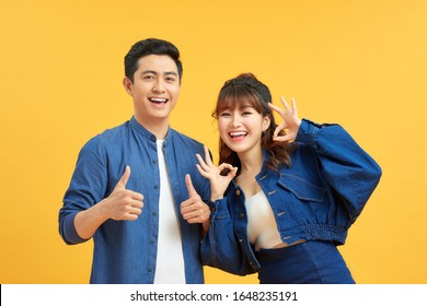 Excited Beautiful Asian Couple Shows Thumb Up Gesture Agree To Do Something And Collaborate Against Orange Wall, Did Great Job, Show Approval, Like Idea. Everything Will Be OK.