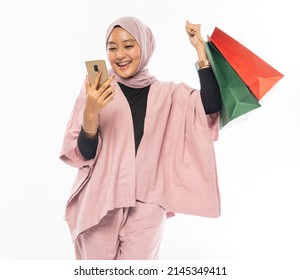 excited beautiful asian muslim woman with hijab, raise her arm while holding shopping bag - Powered by Shutterstock