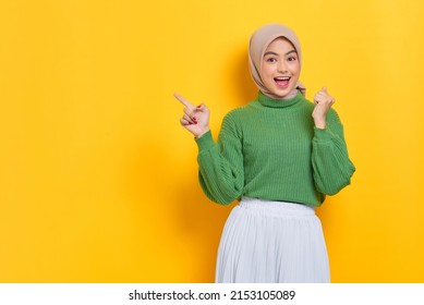 Excited beautiful Asian woman in green sweater pointing fingers aside at copy space isolated over yellow background - Powered by Shutterstock