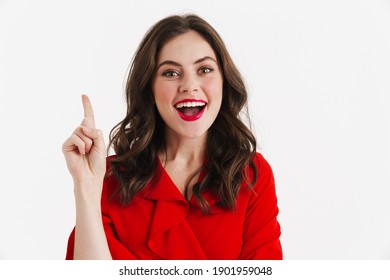 Excited beautiful girl wearing red dress posing pointing finger upward isolated over white background