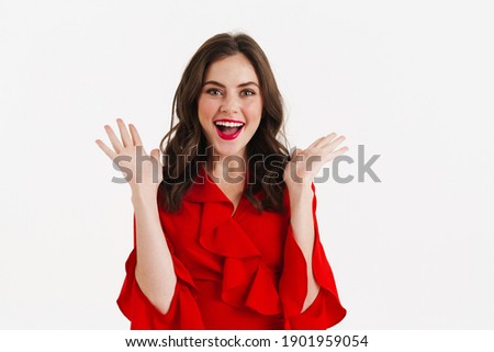 Excited beautiful girl wearing red dress posing on camera isolated over white background