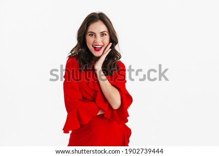Excited beautiful girl wearing red dress posing on camera isolated over white background