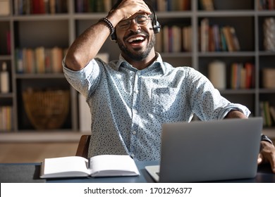 Excited biracial male call center agent in headset have fun laugh working on computer online, overjoyed African American man busy studying or watching funny training webinar on computer gadget