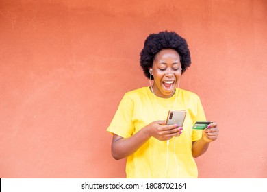 Excited Black African Young Woman Shopping Online Holding Credit Card Using Modern Mobile Phone