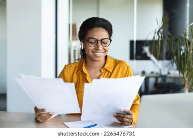 Excited black businesswoman reading papers and positive business report, sitting at workplace in modern office interior. Successful entrepreneurship career, accounting and documentation - Powered by Shutterstock