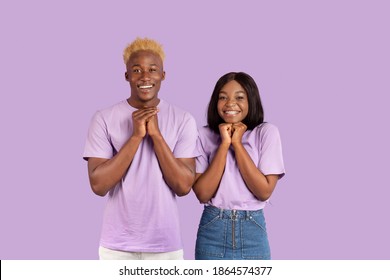 Excited Black Couple Anticipating Something Wonderful, Making Wish, Begging Or Praying Over Violet Studio Background. Hopeful African American Guy And His Girlfriend Wishing For Good Luck