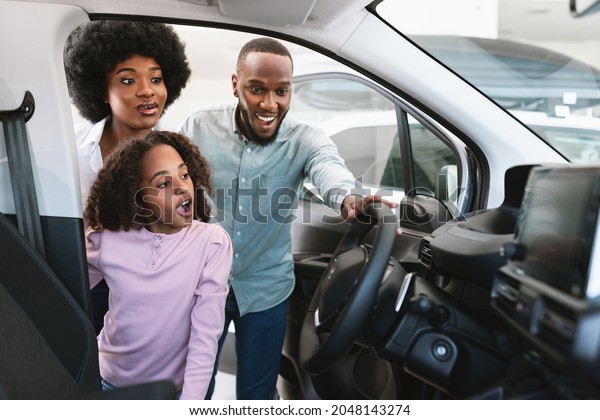 Excited\
black family looking into car salon, selecting new automobile at\
dealership, copy space. African American clients checking auto\
before rental or purchase, going on test\
drive