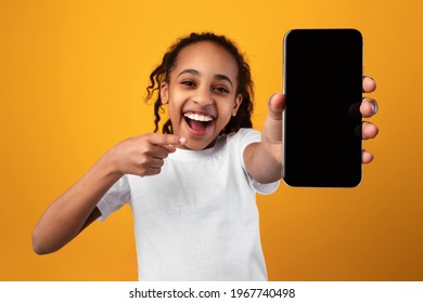 Excited Black Girl Pointing At Phone Blank Screen Showing Smartphone To Camera Recommending Application Over Yellow Studio Background. Great Mobile App For Cellphone Concept. Mockup - Powered by Shutterstock