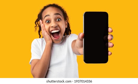 Excited black girl showing blank empty smartphone screen for mockup