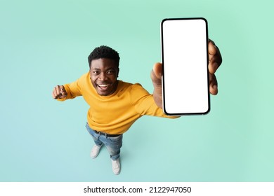 Excited Black Guy Demonstrating Smartphone With Blank White Screen, Showing Free Copy Space For Your Ad, Recommending Mobile App Or Website, Standing Over Blue Background, Mockup