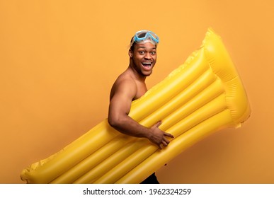 Excited black guy in snorkeling mask holding inflatable lilo, walking to beach on yellow studio background. African American diver with pool float ready for deep water swimming