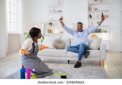 Excited Black Guy Watching Football On TV, Happy Over Victory Of His Team, Angry Wife Cleaning House Alone, Feeling Offended With Her Husband's Laziness. Family Conflicts Over Domestic Chores