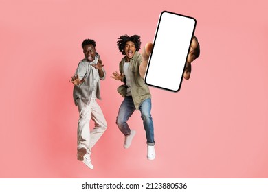 Excited Black Male Friends Jumping And Demonstrating Smartphone With White Blank Screen, African American Guys Offering App Or Website, Pink Studio Background, Mockup Collage Banner
