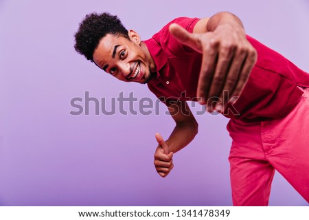 Excited black male model dancing in studio. Funny emotional man in red t-shirt looking to camera with smile.