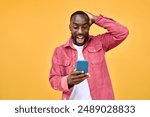 Excited Black man looking at smartphone with wow reaction isolated on yellow. Happy African young gen z guy holding cellphone reading message on cell phone. Amazed user winner using mobile phone