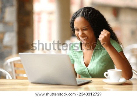 Excited black woman checking good news on laptop in a bar terrace