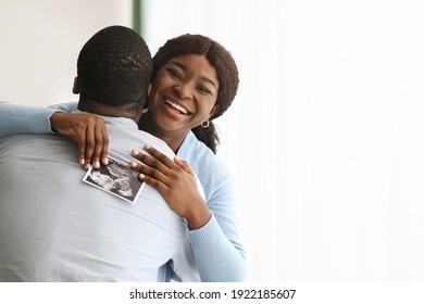 Excited black woman holding ultrasound image and hugging her man, copy space. Happy african american couple future parents embracing, got good news about pregnancy, home interior - Powered by Shutterstock