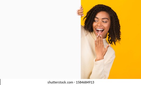 Excited Black Woman Looking Over Copy Space, Hiding Behind Blank Billboard, Peeking Out White Placard