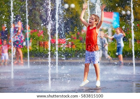 excited boy having fun between water jets, in fountain. Summer in the city