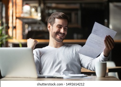 Excited business man student reading postal mail letter overjoyed by great news, happy male winner holding paper bill with loan approval celebrate taxes refund receive salary rise payment sit at desk