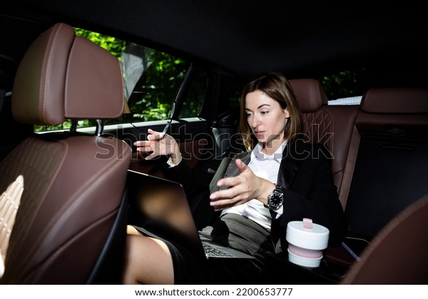 Excited business woman\
sits on the backseat of her car, works on laptop and going to\
business deal meeting