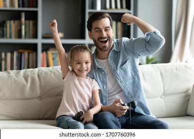 Excited by videogame victory little kid girl and her father raised hands scream with joy sit on sofa at home. Father his small daughter holds playing celebrate success feels happy - Powered by Shutterstock