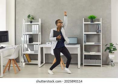 Excited carefree business woman holding office papers, dancing and having fun during break at work.Funny happy modern short haired active young girl feeling free from responsibility as vacation starts
