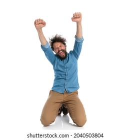 excited casual man standing on his knees and celebrating succes on white studio background