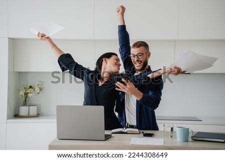 Excited caucasian couple after calculate their year earnings, celebrating successful business at new home using calculator, laptop. Woman raises hands in winner gesture holds papers. Financial freedom Foto d'archivio © 