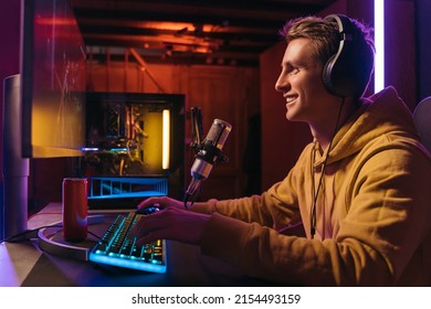  Excited caucasian gamer streamer with headphones playing computer pc video at his living room, recording live stream using microphone, drinking energy drink. Cyber sport and social media concept - Shutterstock ID 2154493159