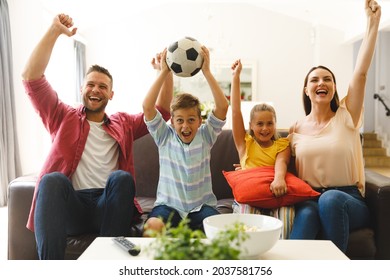 Excited caucasian parents on couch with daughter and son watching football match on tv and cheering. family entertainment and leisure time together at home.