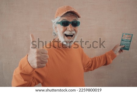 Excited caucasian senior man doesn't believe his eyes holding filled winning lottery ticket and celebrating victory. Lucky happy smiling thumb up elderly man won a jackpot.