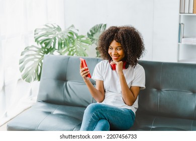 Excited cheerful gen Z female using mobile phone getting surprising good news while playing mobile game on sofa. - Shutterstock ID 2207456733