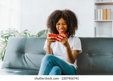 Excited cheerful gen Z female using mobile phone getting surprising good news while playing mobile game on sofa. - Shutterstock ID 2207456741