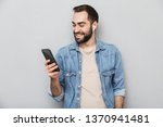 Excited cheerful man wearing shirt isolated over gray background, wearing earphones, using mobile phone